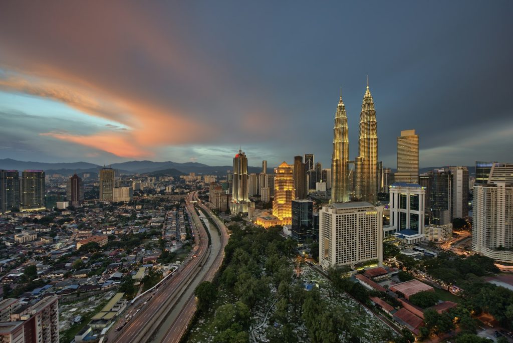 Cityscape of Kuala Lumpur, Malaysia at dusk, with illuminated Petronas Towers in the distance.